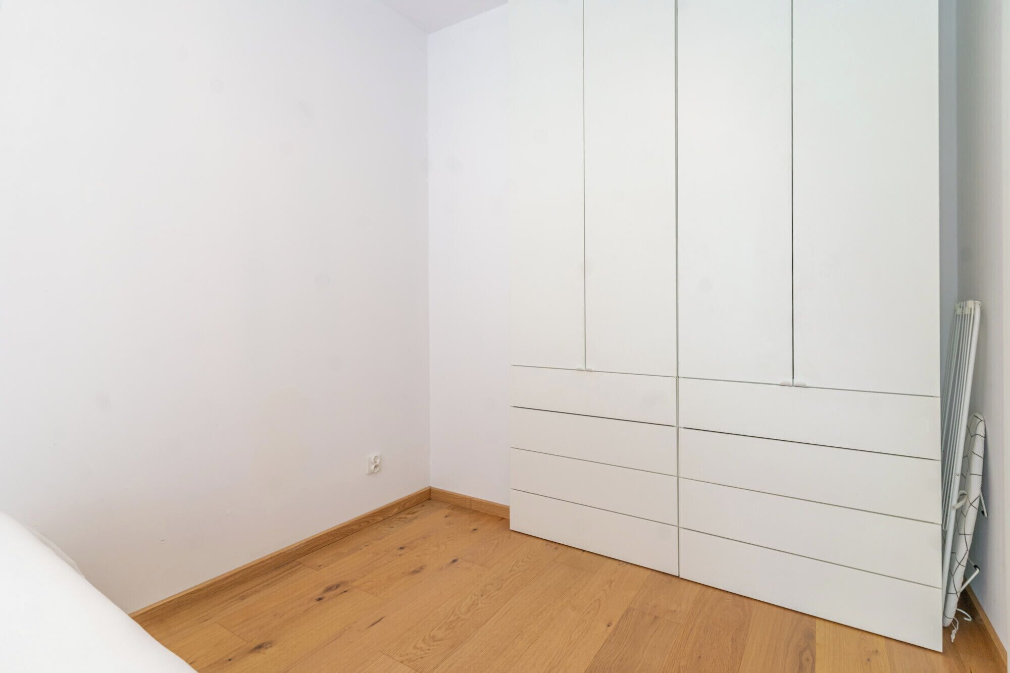 Una habitación con un armario blanco, suelo de madera y un radiador.