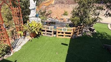 A garden with artificial grass, a wooden fence, a statue, and a pergola.