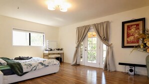 Ein Schlafzimmer mit einem Bett, einem Schminktisch mit Spiegel, einem Schreibtisch und einer Tür, die auf einen Balkon führt.