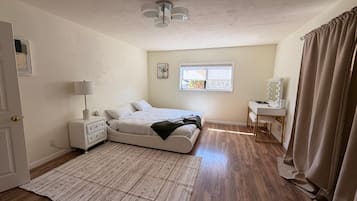 Ein Schlafzimmer mit Bett, Nachttisch, Lampe, Fenster und Schminktisch mit Spiegel.
