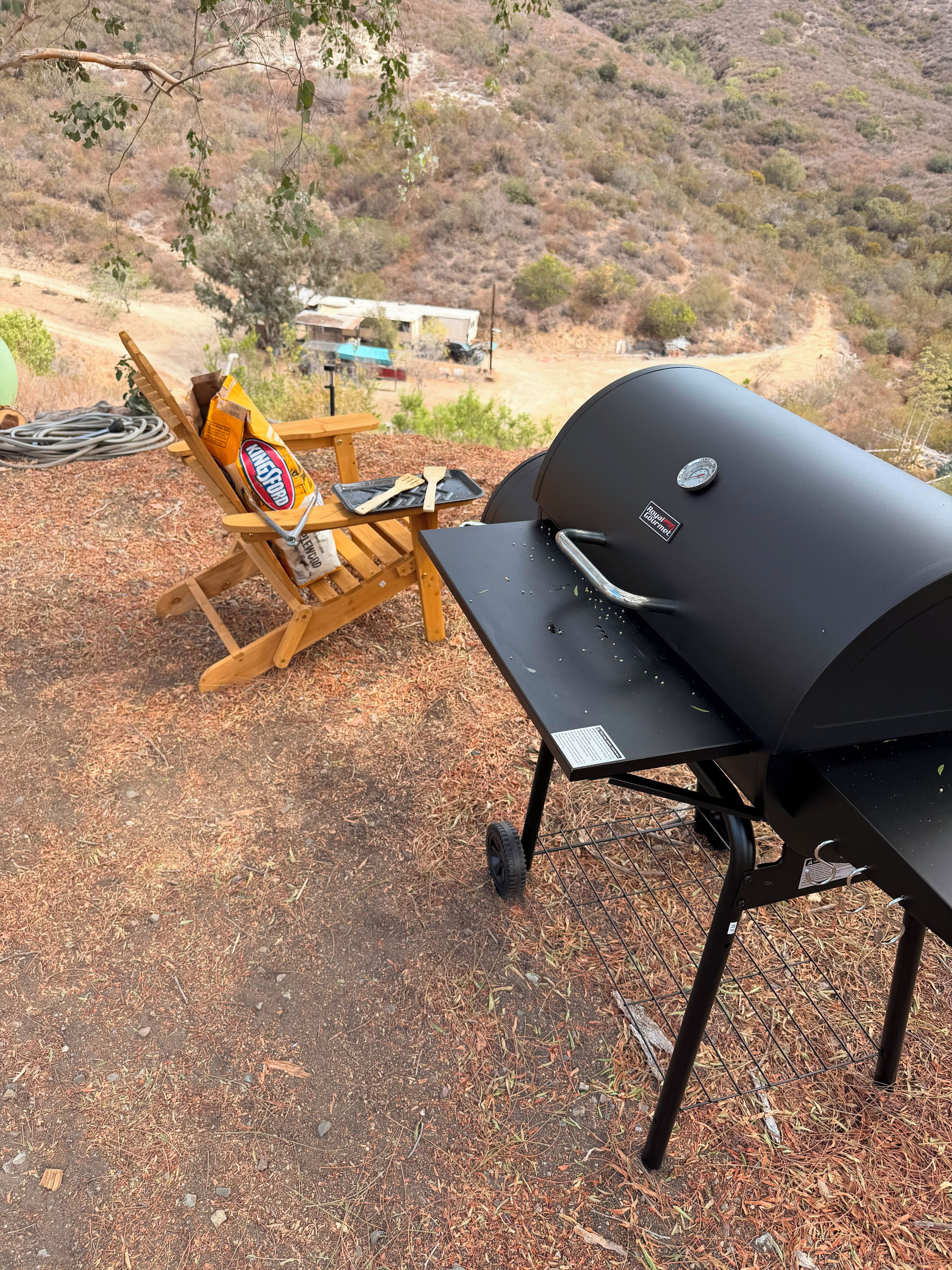 Ein tragbarer Grill mit Firmenlogo, ein Holzstuhl mit einer Tüte Chips und eine Metall-Grillpfanne.