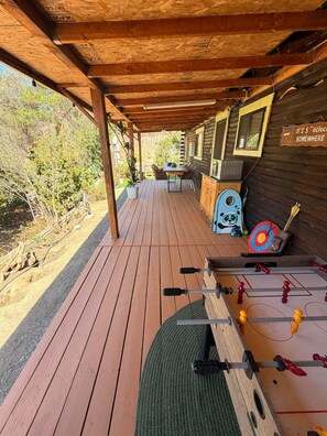 Una terraza de madera con mesa de fútbol, una mesa con sillas y una laptop sobre una pared de madera.