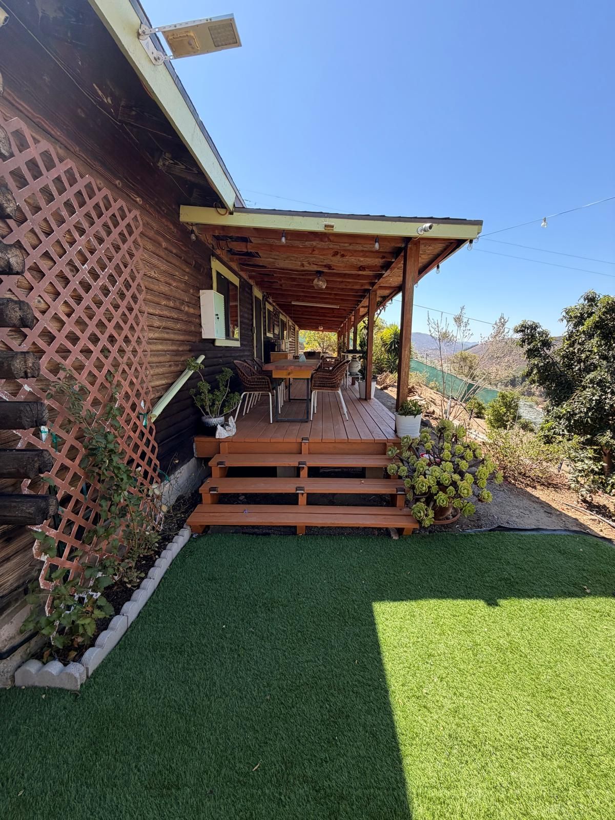 Um deck de madeira com pérgola, uma pequena área de estar ao ar livre e um gramado bem cuidado.