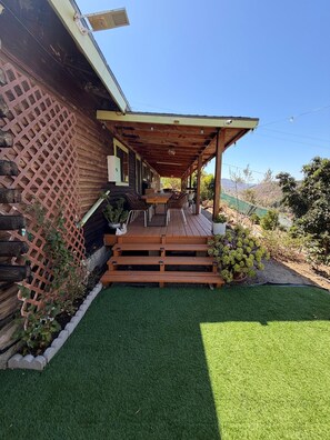 Una terraza de madera con pérgola, un pequeño espacio de estar al aire libre y un césped bien cuidado.