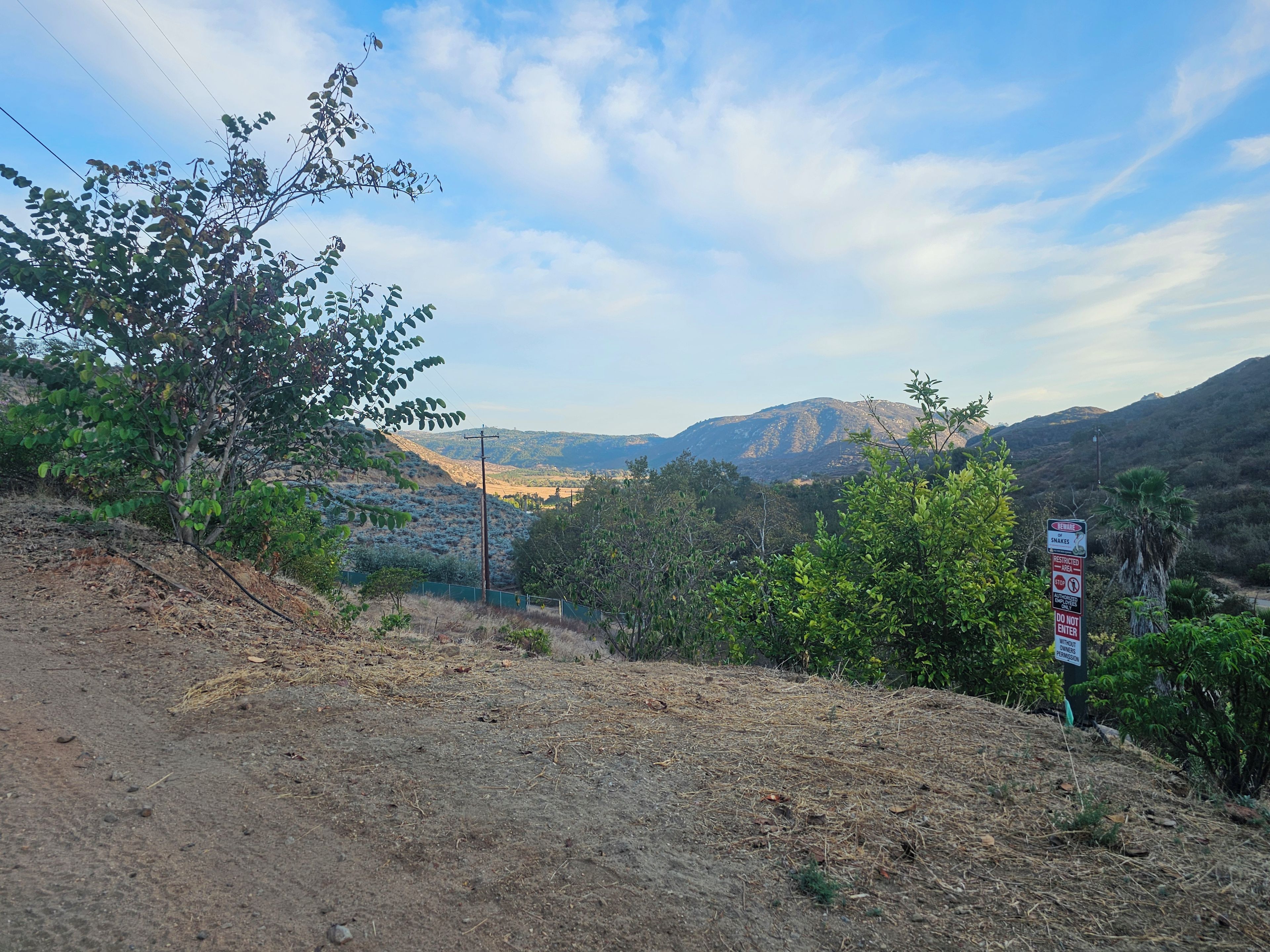 A dirt path leading to a mountainous landscape with a sign warning of snakes.