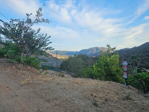 Sendero de tierra que conduce a un paisaje montañoso, con un letrero que advierte sobre serpientes.
