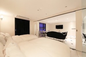 A modern bedroom with a large bed, a black bathtub, and a television on the wall.