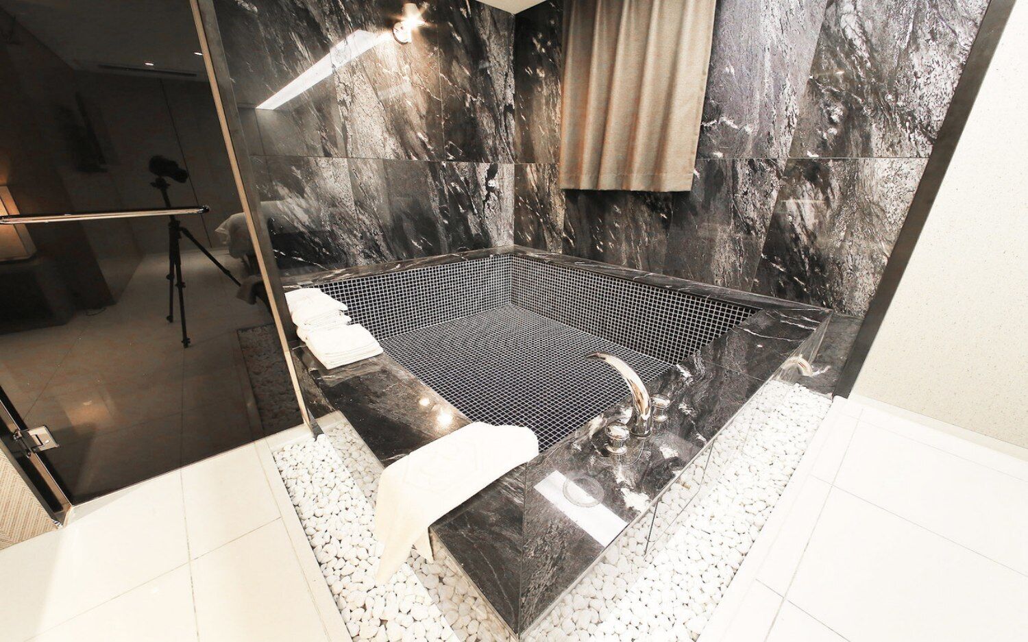 A modern bathroom with a black marble wall, a glass shower enclosure, and a white tiled floor.