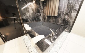 Un baño moderno con pared de mármol negro, cabina de ducha de vidrio y suelo de baldosas blancas.