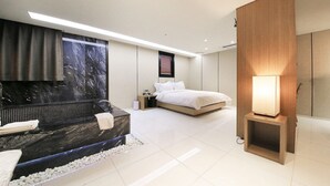 Une chambre à coucher moderne avec une baignoire en marbre, un lit, une table de chevet et une lampe fixée au mur.