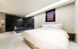 Una habitación de hotel moderna con una cama grande, ducha integrada y pared de mármol.