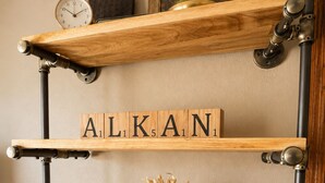 Une étagère en bois, ornée d’une horloge ancienne, d’un tableau encadré et d’un jeu de mots sur l’étagère supérieure.