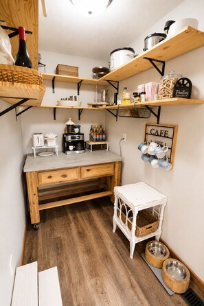 A compact kitchen with wooden shelves, a coffee station, and a pet feeding area.