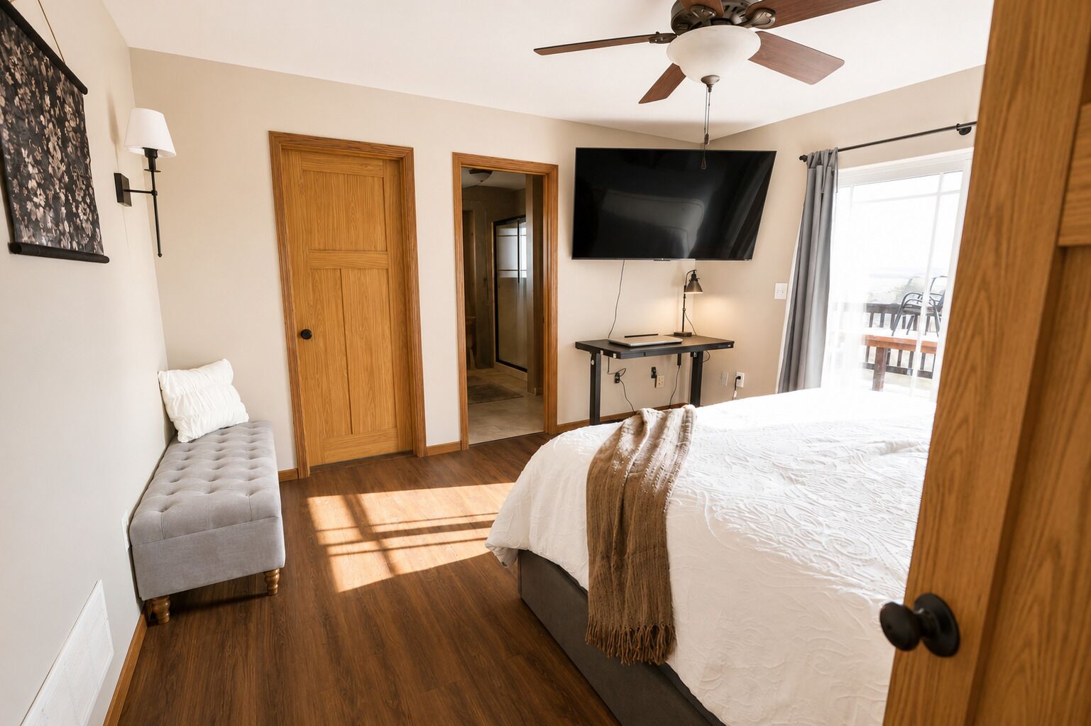Quarto com cama, escrivaninha com televisão, ventilador de teto e porta para outro cômodo.