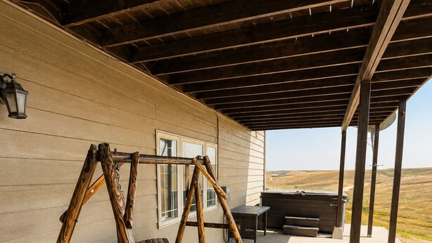Un espace extérieur abrité comprenant une balançoire en bois, un barbecue et une vue sur le paysage.