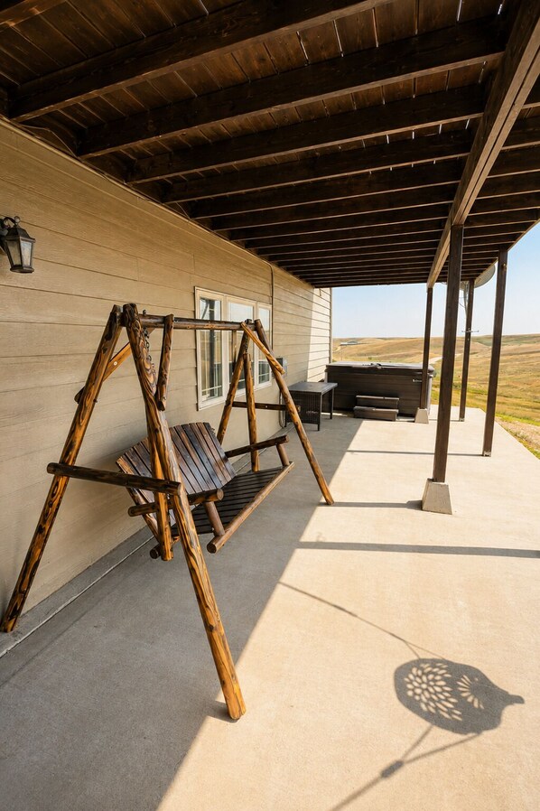 A covered outdoor area with a wooden swing set, a barbecue grill, and a view of the landscape.