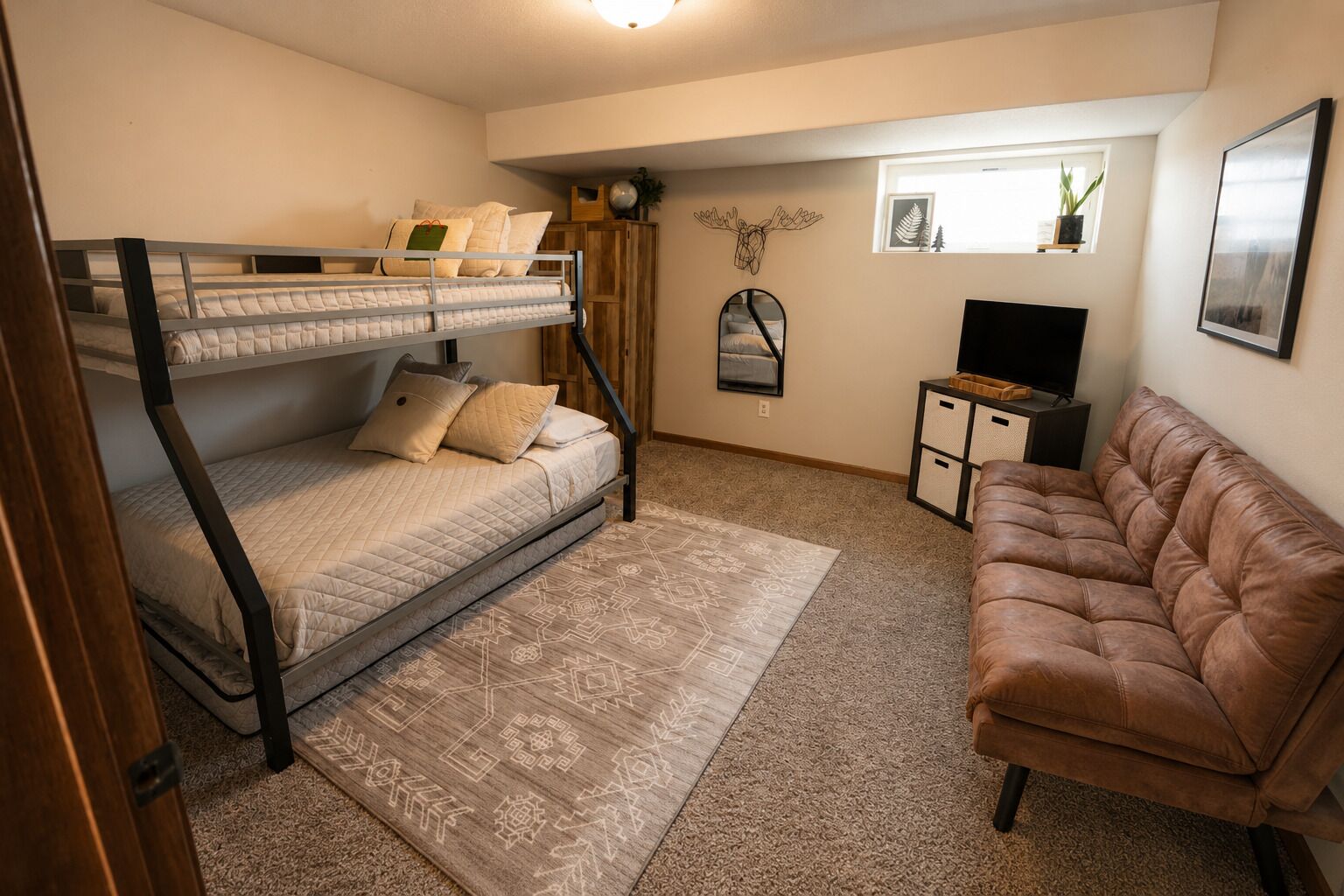 Una habitación con una cama litera, un sofá de cuero marrón, un televisor pequeño y un espejo decorativo.