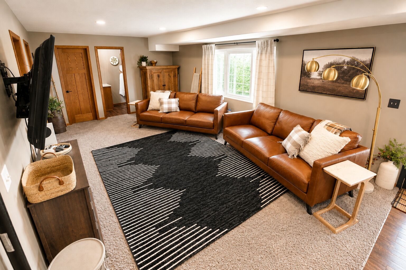 Uma sala de estar com um sofá de couro marrom, um tapete preto e branco, um armário de madeira e um quadro na parede.