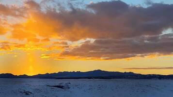 A snowy landscape with a mountain range in the distance and a sunset with clouds.