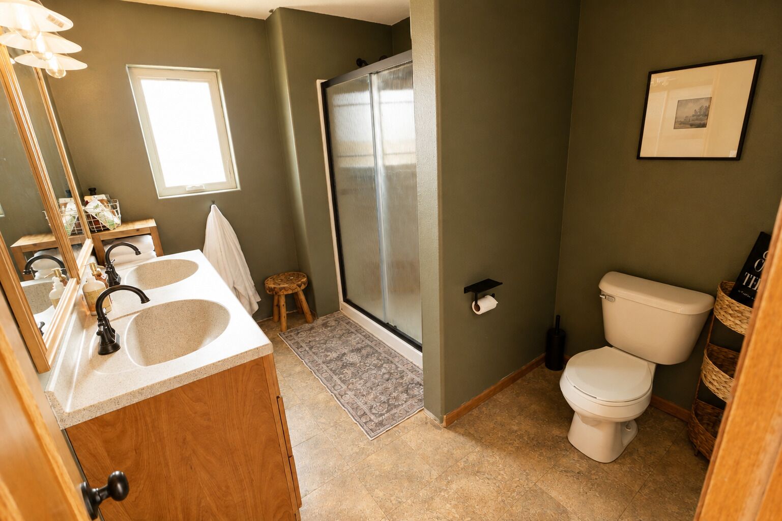 A bathroom with a sink, mirror, toilet, shower, and a small stool.