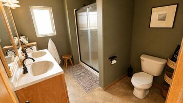 A bathroom with a sink, mirror, toilet, shower, and a small stool.