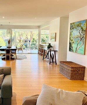 A spacious living area with a wooden floor, a dining table with chairs, a sofa, and a large painting on the wall. - Spacious Avalon Beach family retreat. Walk to beach. (Avalon Beach)