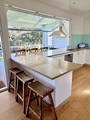 A modern kitchen with a large island, wooden stools, and a view of the outdoors. - Spacious Avalon Beach family retreat. Walk to beach. (Avalon Beach)