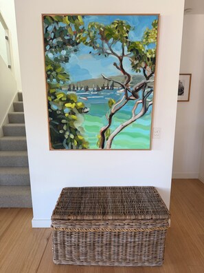 Ein Gemälde zeigt einen Baum, eine Küstenlandschaft, eine Korbsitzbank und eine Treppe.