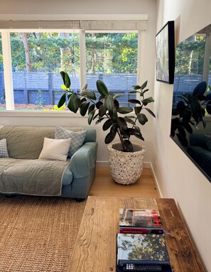 A living room with a sofa, a potted plant, a wooden coffee table, and a bookshelf. - Spacious Avalon Beach family retreat. Walk to beach. (Avalon Beach)