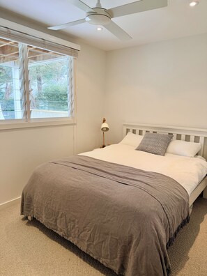 Ein Schlafzimmer mit Bett, Deckenventilator, Fenster mit Jalousien und einer Nachttischlampe.