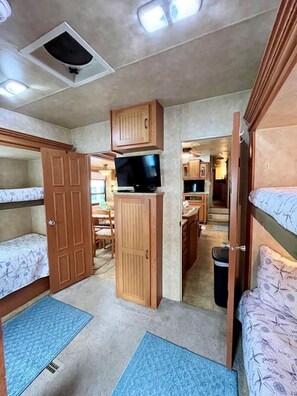 Ein kompaktes Wohnmobil-Interieur mit Etagenbetten, einer Küchenzeile und einem Fernseher.