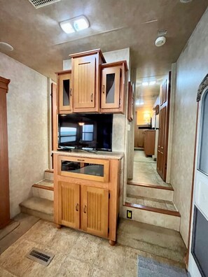 Ein Flur mit Holzausbau, einem Fernseher auf einem Schrank und einem Lüftungsgitter an der Decke.