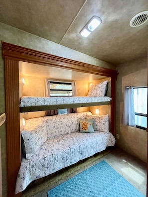 Ein Stockbett mit gemustertem Bettbezug, ein Fenster mit Vorhängen und ein blauer Teppich auf dem Boden.