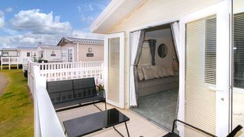 Ein Wohnwagen mit Balkon, einem Bett mit Kopfteil und einem Fenster mit Jalousien.