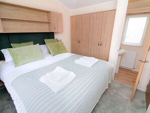 A bedroom with a bed, green pillows, a wooden wardrobe, and a bathroom with a sink and toilet. - Willow's Retreat by Interhome (Lossiemouth)
