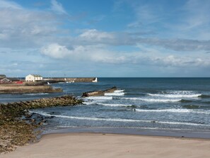 A coastal scene with a sandy beach, rocky shoreline, and a breakwater extending into the sea.