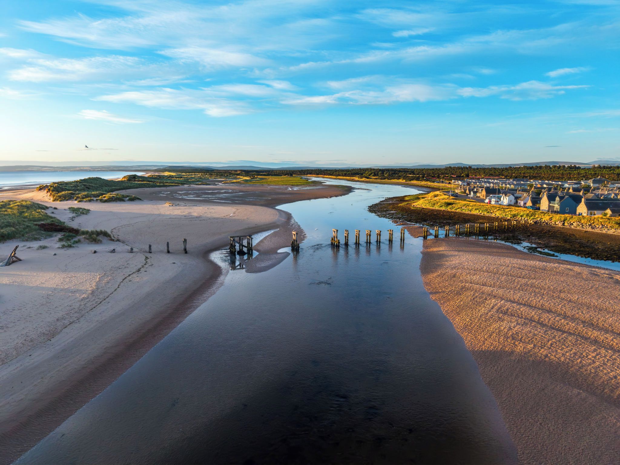 A coastal landscape with a river, sandy beach, and a settlement with buildings.
