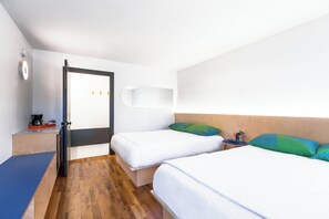 Ett hotellrum med två sängar, ett trägolv, ett skrivbord med en kaffebryggare och en hylla som är monterad på väggen.