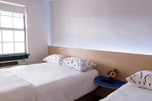 A bedroom with a bed, a nightstand, a window, and a wall-mounted heater.
