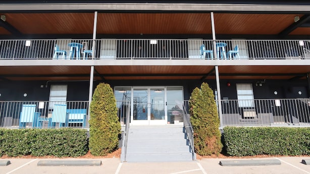 A two-story building with a covered entrance and a balcony with blue chairs. - The Iris Motel - Queen Room (Nashville)