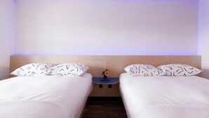 Hotellihuone, jossa on kaksi sänkyä, yöpöytä ja seinään kiinnitetty valaisin.