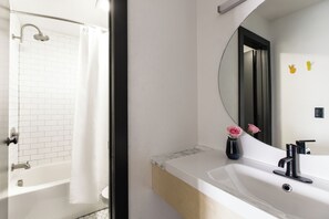 Ein modernes Badezimmer mit einer weißen Badewanne, einem großen Spiegel und einem Waschbecken mit einem schwarzen Wasserhahn.