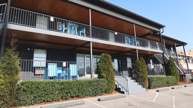 Un edificio de dos pisos con balcón, escaleras y estacionamiento.