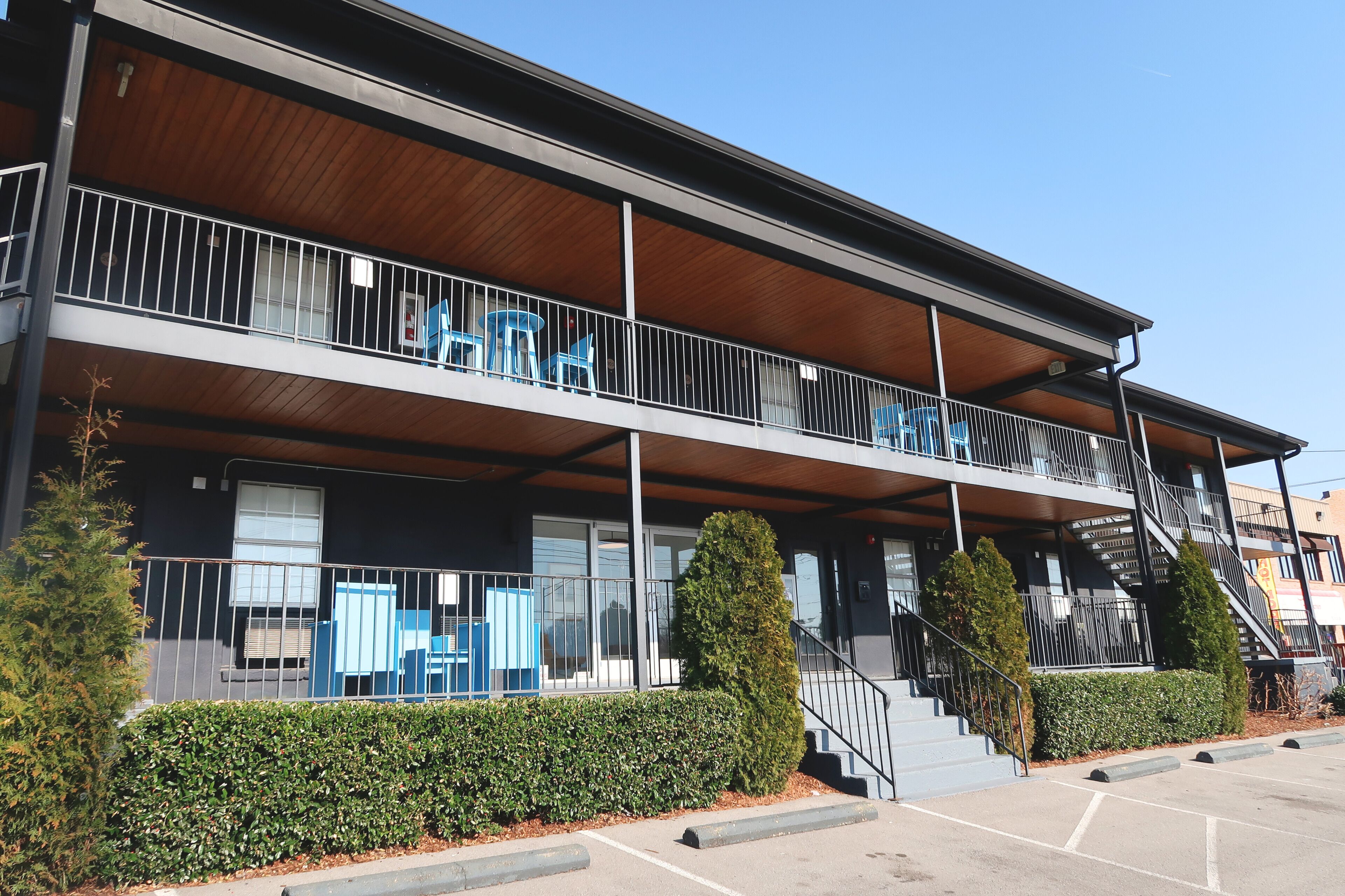 Een gebouw met twee verdiepingen, een balkon, een trap en een parkeerplaats.