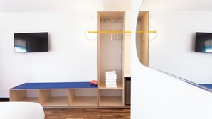 Habitación de hotel moderna con un banco de madera, un armario con espejo y un televisor de pantalla plana en la pared.