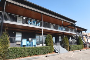 Un edificio de dos pisos con balcón, escaleras y estacionamiento.