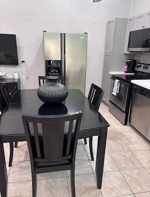 A modern kitchen with a dining table, chairs, a refrigerator, a microwave, and a coffee machine.