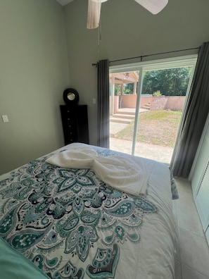 A bedroom with a bed, a dresser, a ceiling fan, and a view of the outdoors.