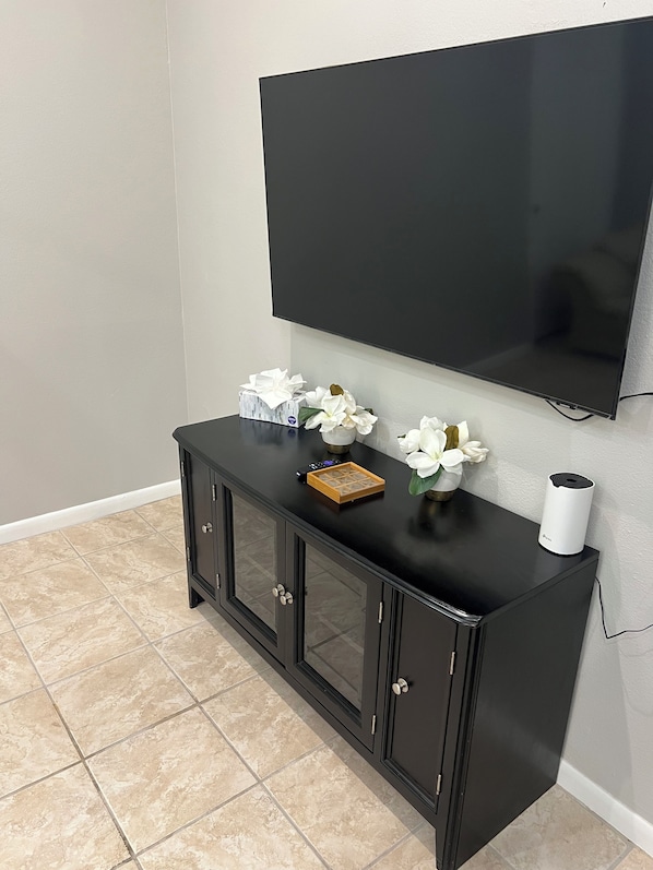 A black TV stand with a flat-screen TV mounted above it, a white tissue box, and a small vase with white flowers.