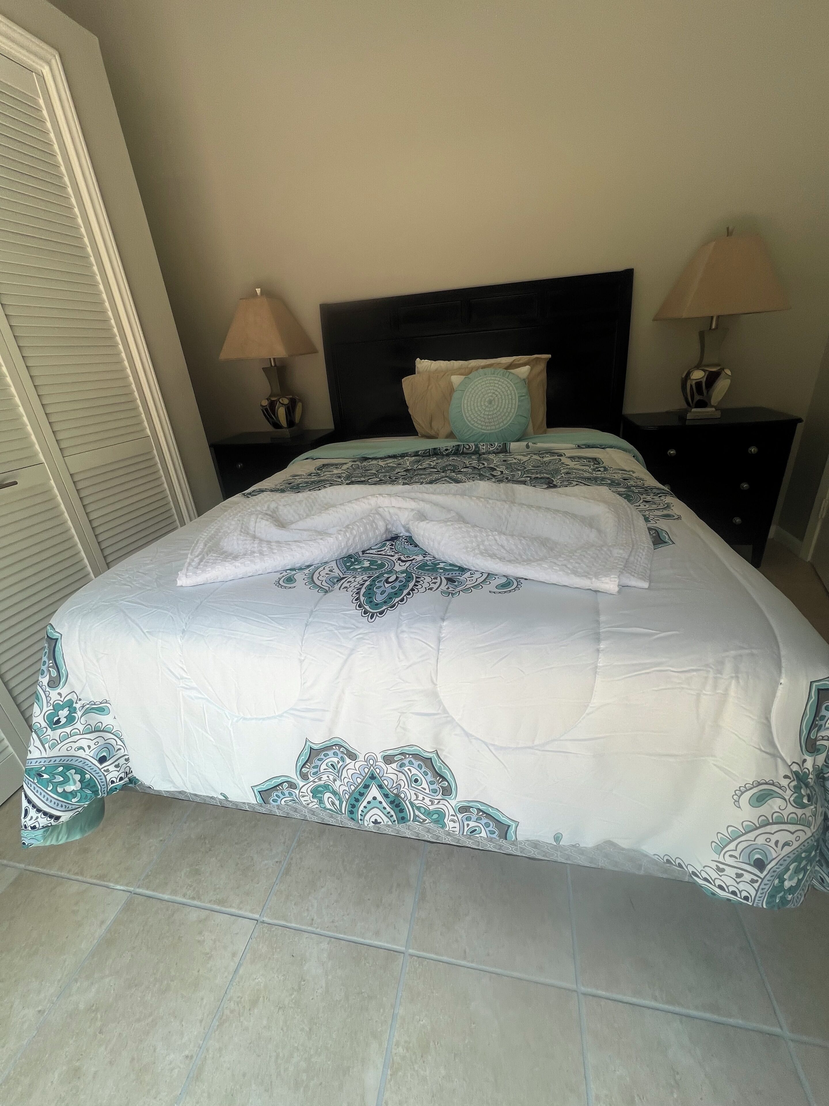 A neatly made bed with a patterned bedspread, two bedside tables with lamps, and a closed door.